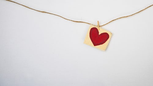 A drawing of a little red heart hanging on a brown string on a white wall
